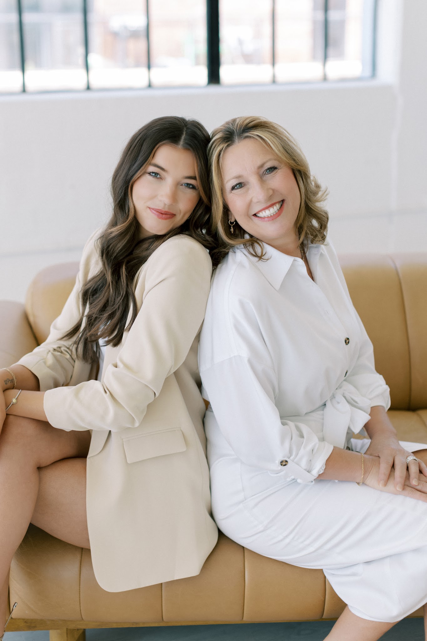 Two women seated together on a sofa in a bright interior.